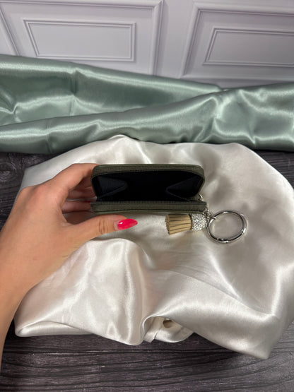 The Little Mermaid miniature book coin purse held open to show its black interior compartment, zippered closure, and attached keyring with tassel.