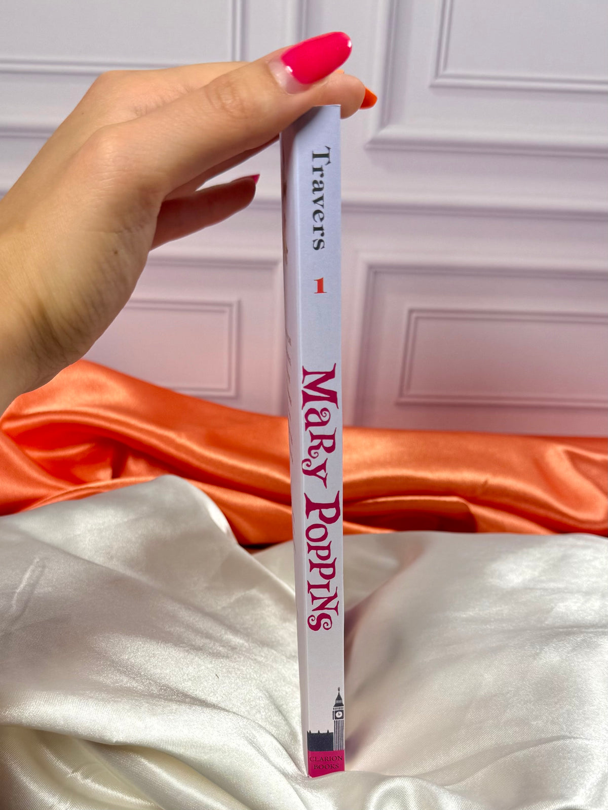 Side view of a Mary Poppins book paperback collection showing the colorful book spine displayed on ivory and red satin fabric.