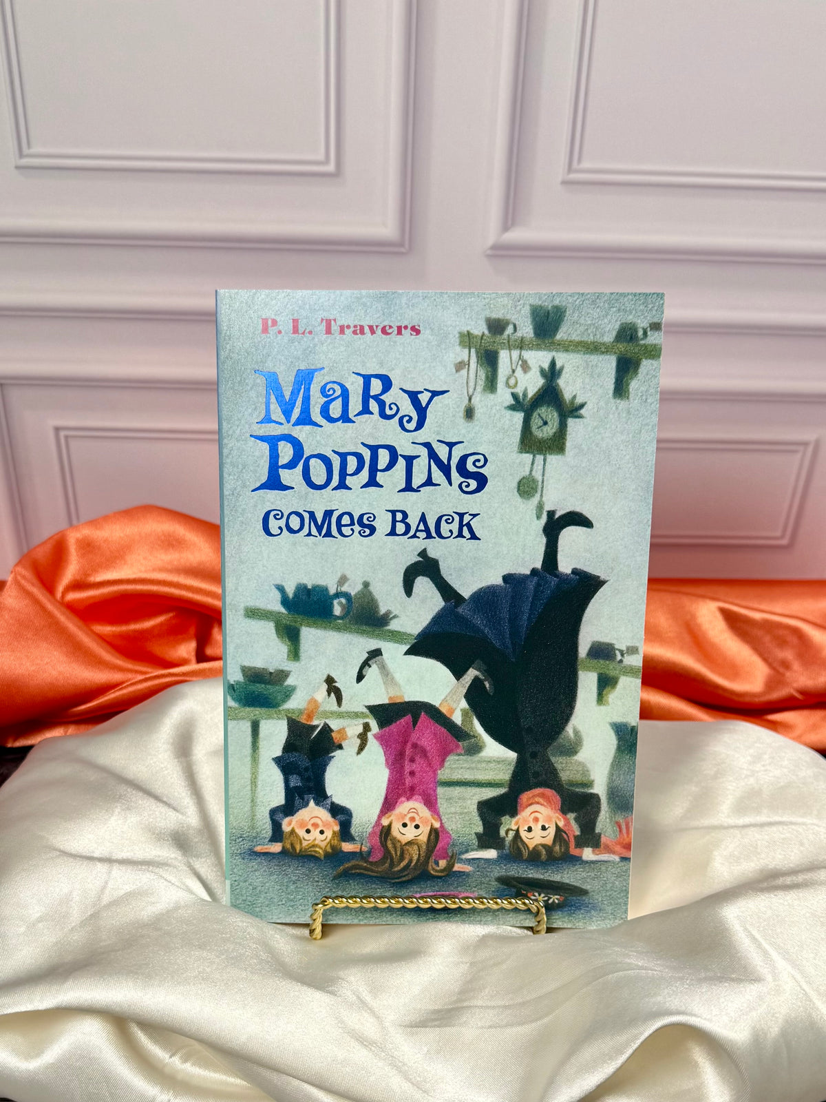 Another illustrated Mary Poppins paperback from the four-book collection, displayed upright against a white paneled background with red satin fabric.