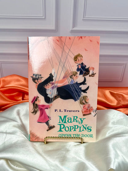 Another illustrated Mary Poppins Opens the Door paperback from the four-book collection, displayed upright against a white paneled background with red satin fabric.
