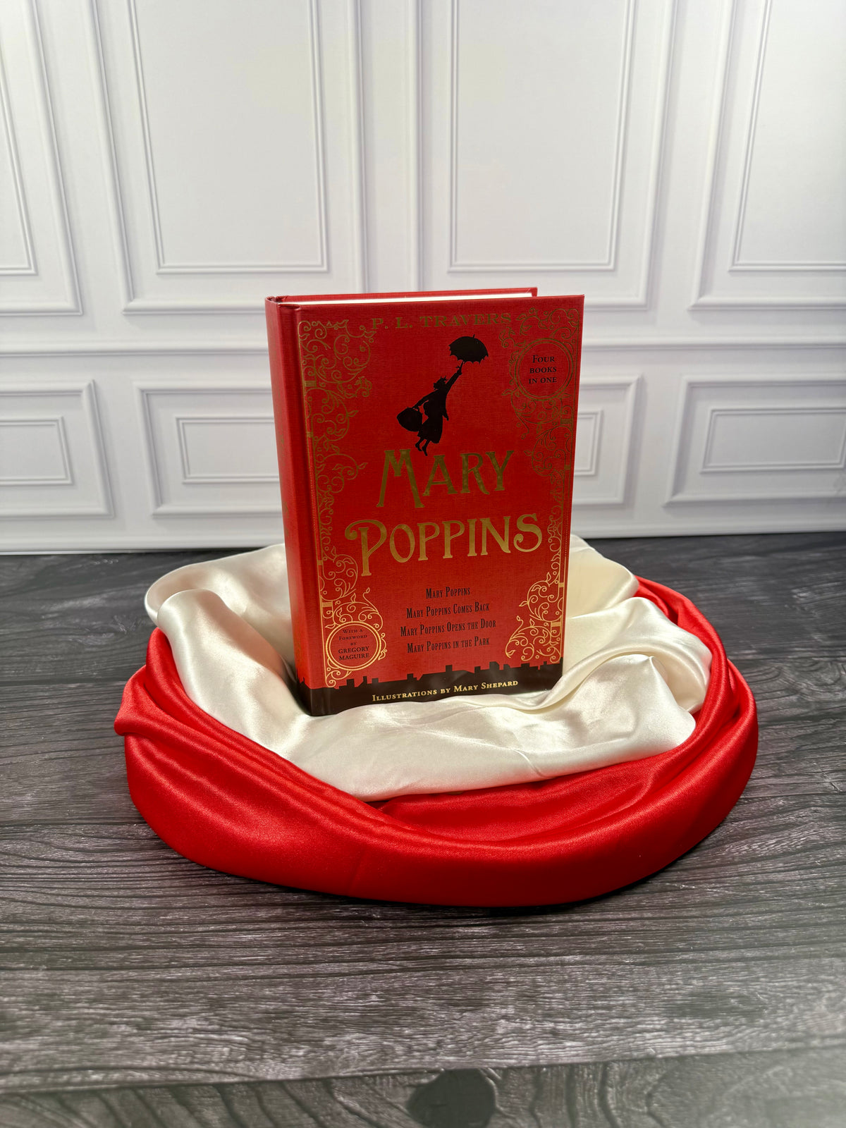 Mary Poppins Collection hardcover treasury by P. L. Travers, red decorative cover displayed on a black book stand with red and ivory satin fabric.