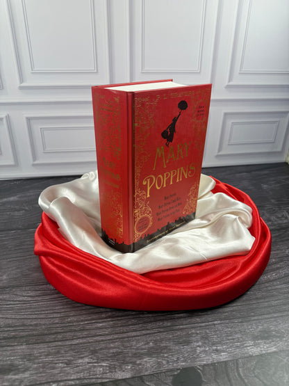 Angled view of the red Mary Poppins Collection hardcover treasury showing its decorative cover and thick binding on a satin-draped book stand.