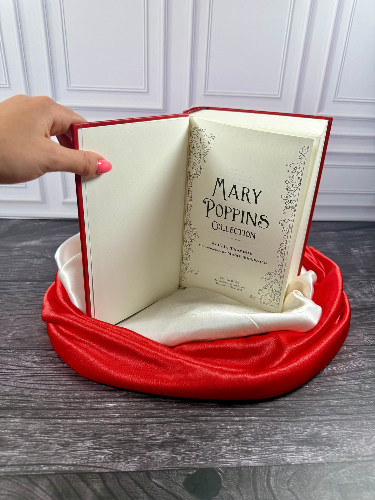 Mary Poppins Collection hardcover treasury opened to its interior pages, displayed on a black book stand with red and ivory satin fabric.