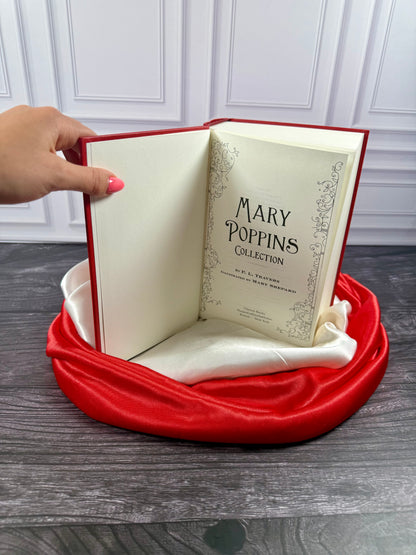 Mary Poppins Collection hardcover treasury opened to its interior pages, displayed on a black book stand with red and ivory satin fabric.