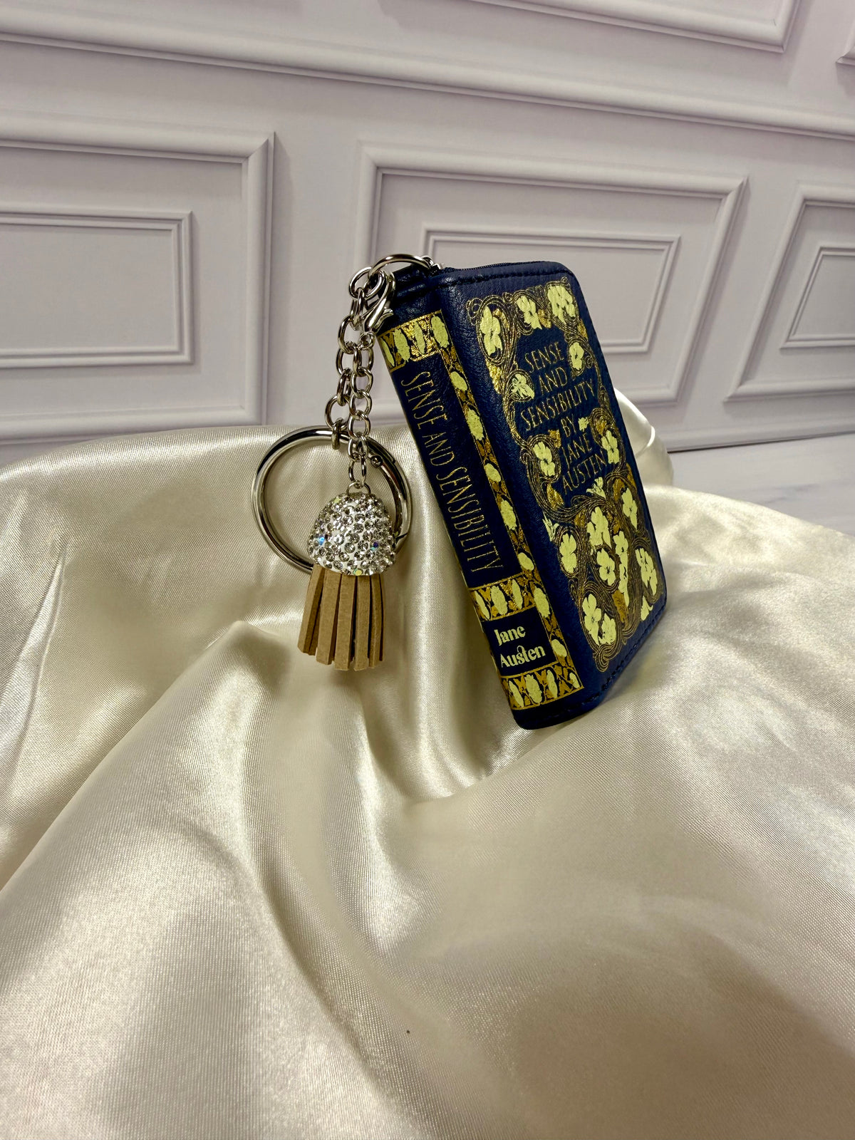 Angled view of Sense and Sensibility miniature book coin purse showing its decorated spine, navy blue cover, gold floral details, and keychain attachment.