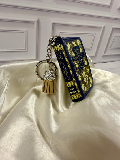 Angled view of Sense and Sensibility miniature book coin purse showing its decorated spine, navy blue cover, gold floral details, and keychain attachment.