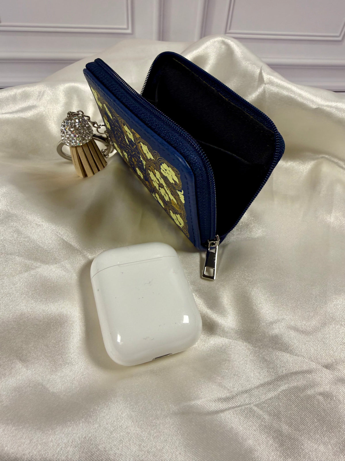 Sense and Sensibility miniature book coin purse opened to show its black interior compartment and zippered closure, with an earbud case nearby for size comparison.