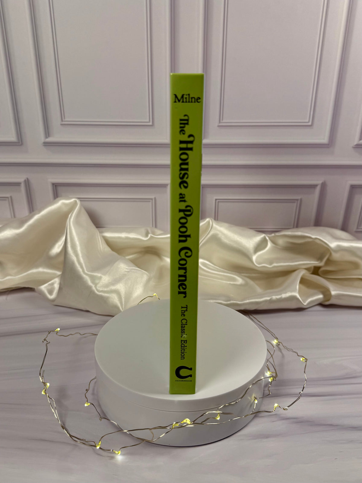 The House at Pooh Corner illustrated hardcover displayed at an angle, showing the green book cover and spine in a styled photograph.