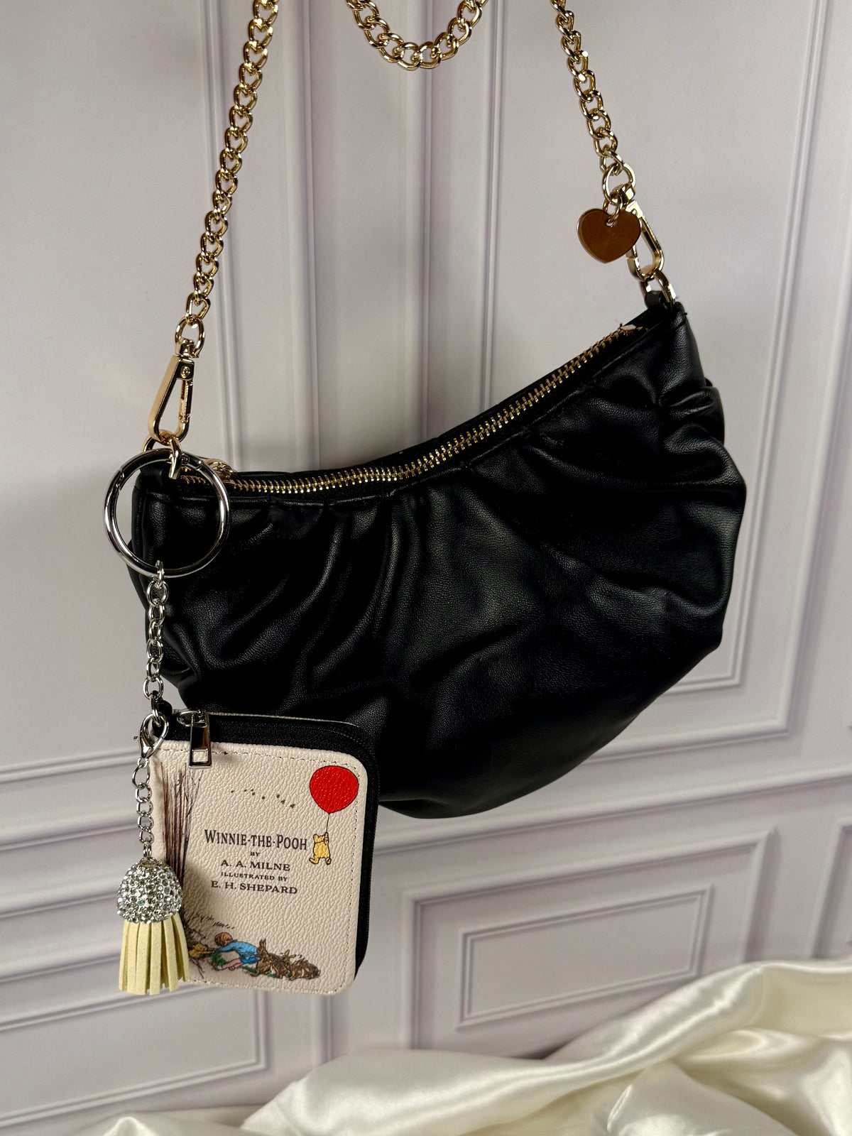 Winnie the Pooh miniature book coin purse bag charm hanging from a black handbag with gold chain, featuring a red balloon cover and cream tassel.