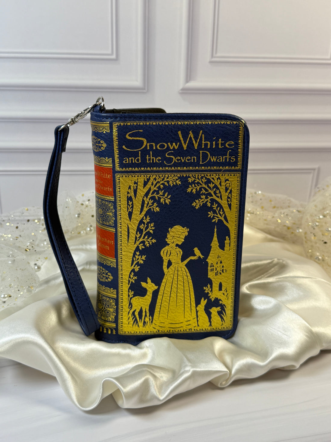 Snow White book wallet in navy vinyl with gold fairytale artwork and detachable wristlet strap.