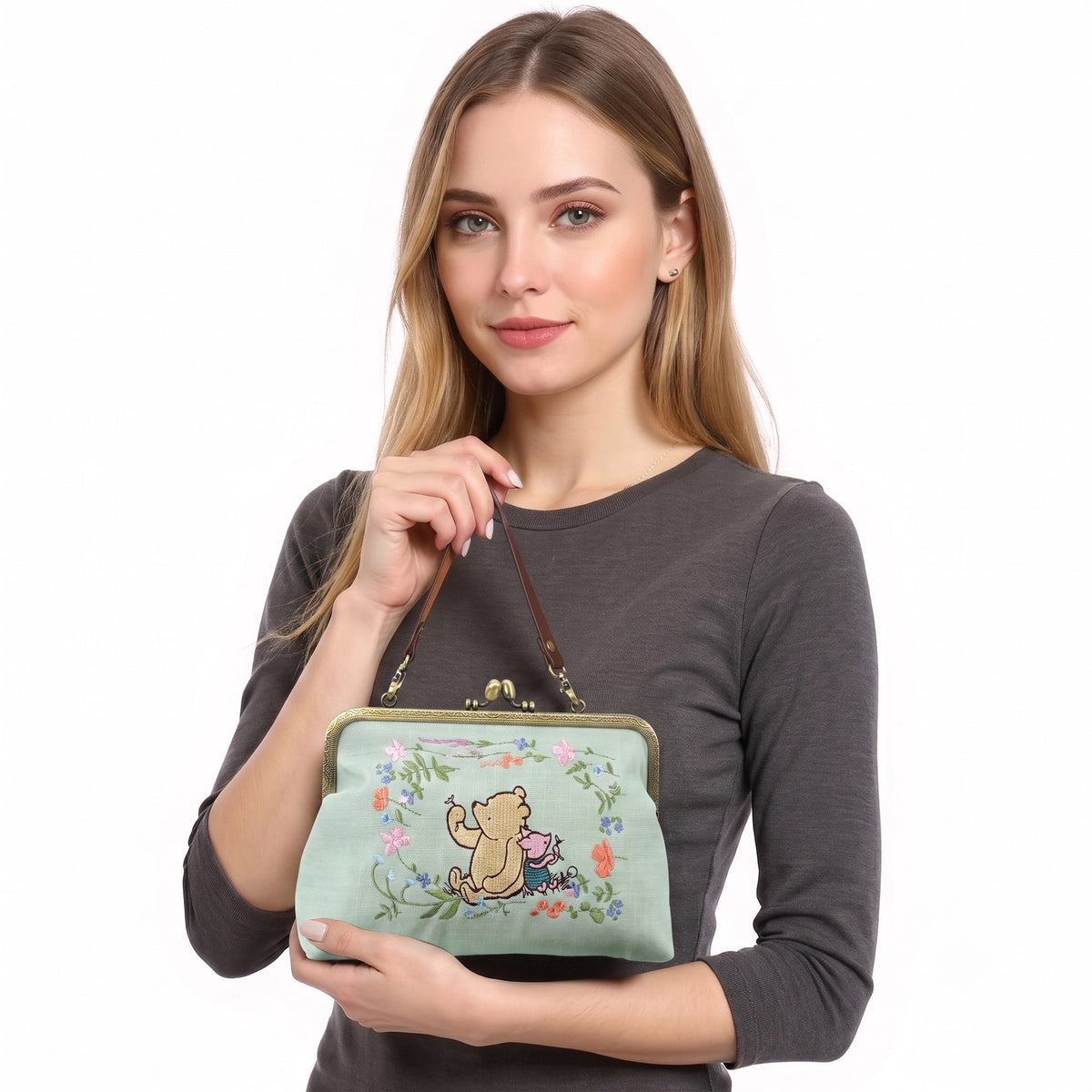 Model holding the mint green Winnie-the-Pooh and Piglet embroidered kisslock handbag, showing its size and detachable wrist strap.