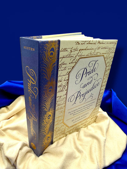 Angled view of the Pride and Prejudice deluxe edition hardcover standing on gold satin, showing its decorative blue and gold binding.