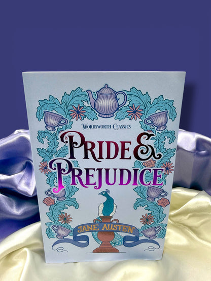 Pride and Prejudice by Jane Austen, Wordsworth Classics paperback with a colorful illustrated cover in blue, turquoise, and purple, displayed on satin fabric.