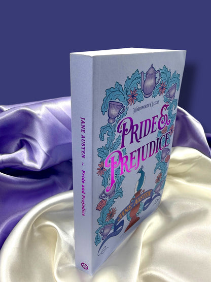 Angled view of Pride and Prejudice by Jane Austen, Wordsworth Classics paperback standing against purple satin fabric, showing its illustrated front cover and spine.