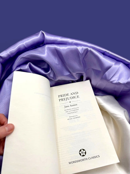 Open Pride and Prejudice Wordsworth Classics paperback showing its interior title page and printed pages against purple satin fabric.