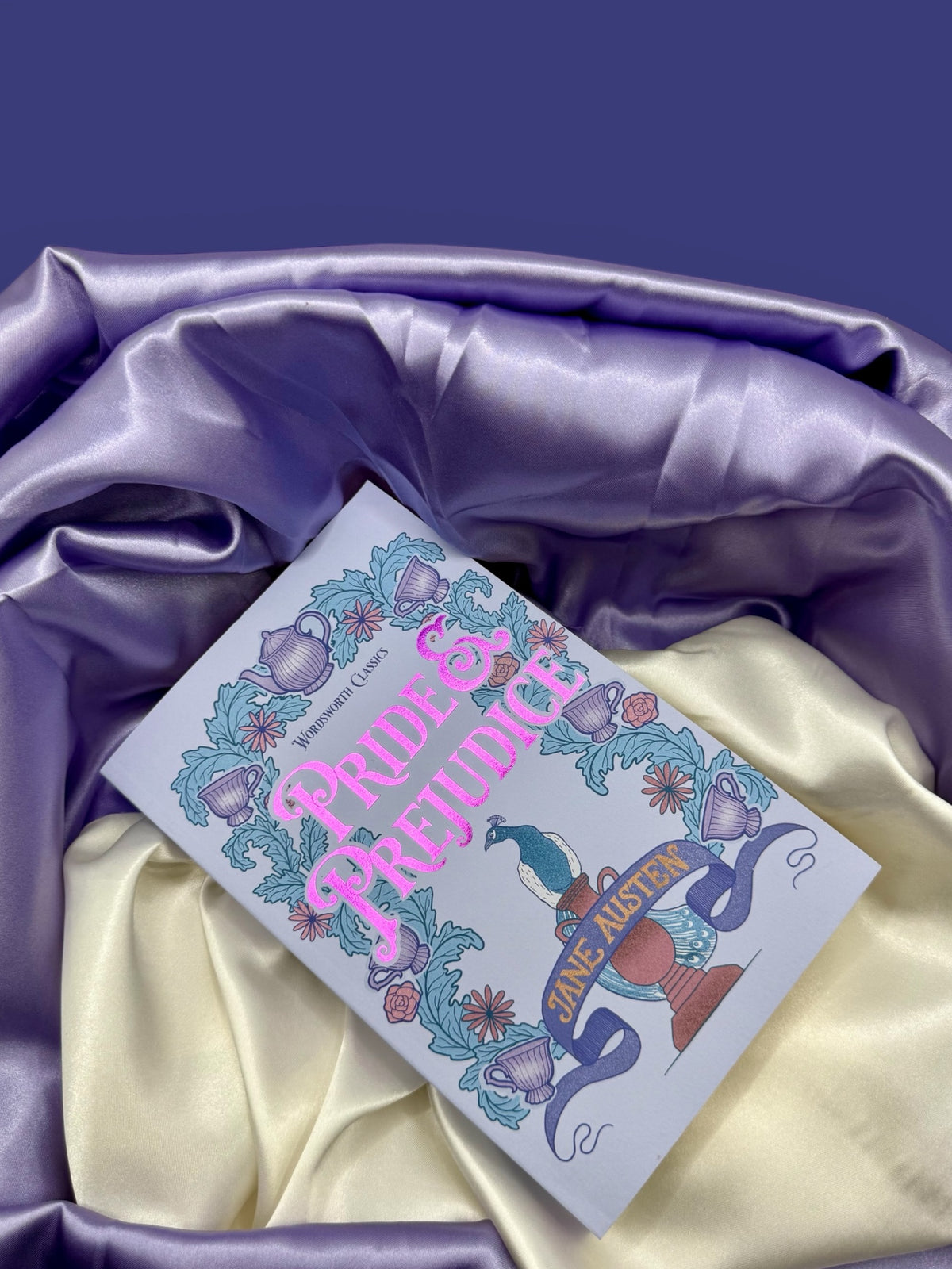 Pride and Prejudice by Jane Austen paperback photographed at an angle on dark purple fabric, highlighting its decorative illustrated cover.