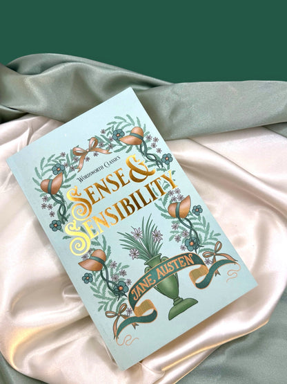 Sense and Sensibility by Jane Austen paperback resting on ivory satin, highlighting its mint-green cover and decorative botanical artwork.
