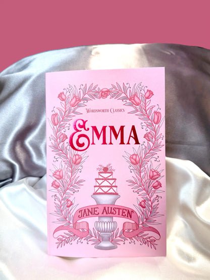 Emma by Jane Austen, Wordsworth Classics paperback with a decorative pink illustrated cover, photographed against soft satin fabric.