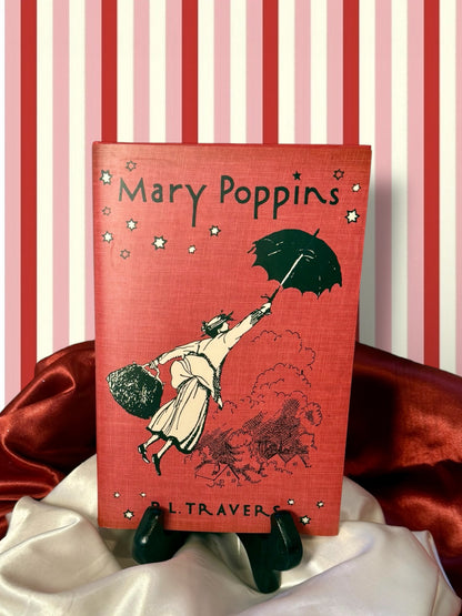 Mary Poppins by P. L. Travers, classic jacketed hardcover edition featuring red cover artwork of Mary Poppins floating through the air beneath her umbrella.