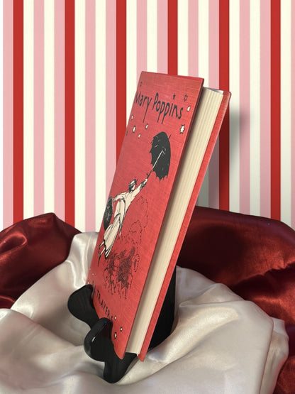 Side page edge and front view of the Mary Poppins hardcover edition by P. L. Travers, displayed on a book stand with red satin fabric.