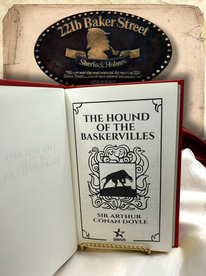 Interior title page of The Hound of the Baskervilles by Sir Arthur Conan Doyle featuring a black hound illustration, ornamental border, and Sirius publisher emblem.