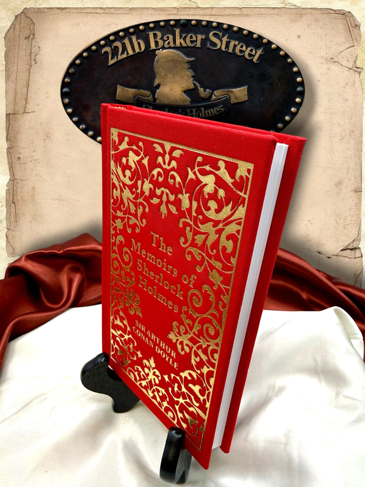 Three-quarter view of The Memoirs of Sherlock Holmes hardcover showing its bright red cloth binding, intricate gold cover design, and white page edges.