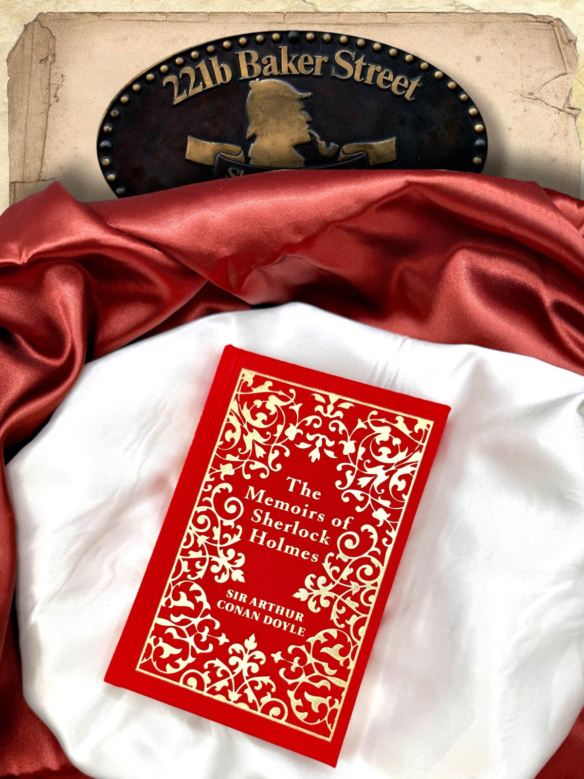 The Memoirs of Sherlock Holmes red and gold clothbound hardcover photographed flat on ivory satin with red fabric and a Sherlock Holmes 221B Baker Street sign.