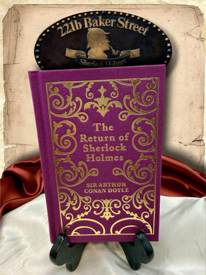 Close-up of the purple cloth cover and intricate gold ornamental design on The Return of Sherlock Holmes hardcover by Sir Arthur Conan Doyle.