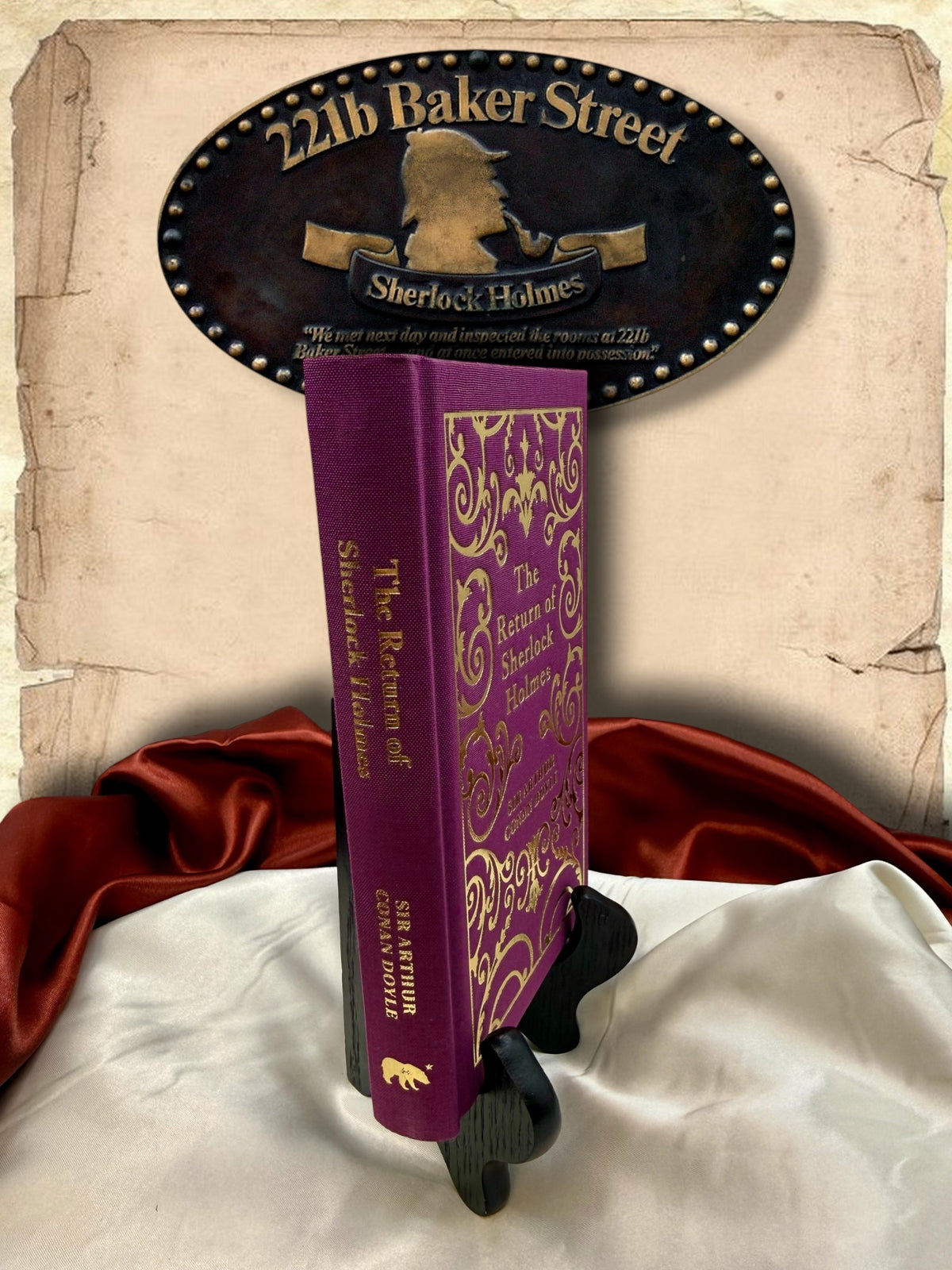 Angled view of The Return of Sherlock Holmes clothbound hardcover showing its purple spine, gold lettering, decorative front cover, and author name.