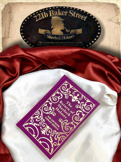 The Return of Sherlock Holmes purple and gold clothbound hardcover photographed flat on ivory satin with red fabric and a 221B Baker Street Sherlock Holmes sign.