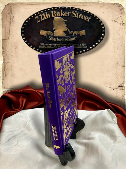 Angled spine view of His Last Bow purple clothbound hardcover, showing gold title and author lettering, decorative front cover, and small gold publisher emblem.