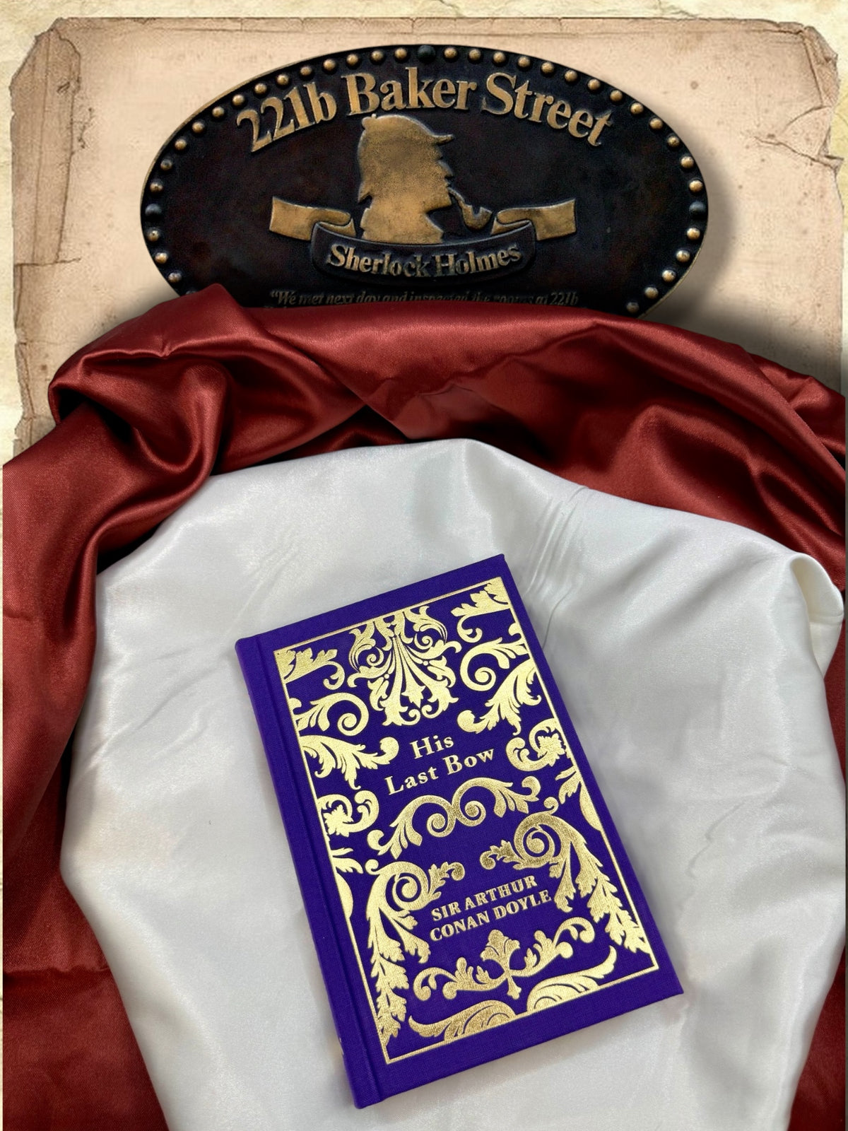 His Last Bow by Arthur Conan Doyle photographed flat on ivory satin with red fabric, highlighting the purple cloth hardcover and intricate gold ornamental design.