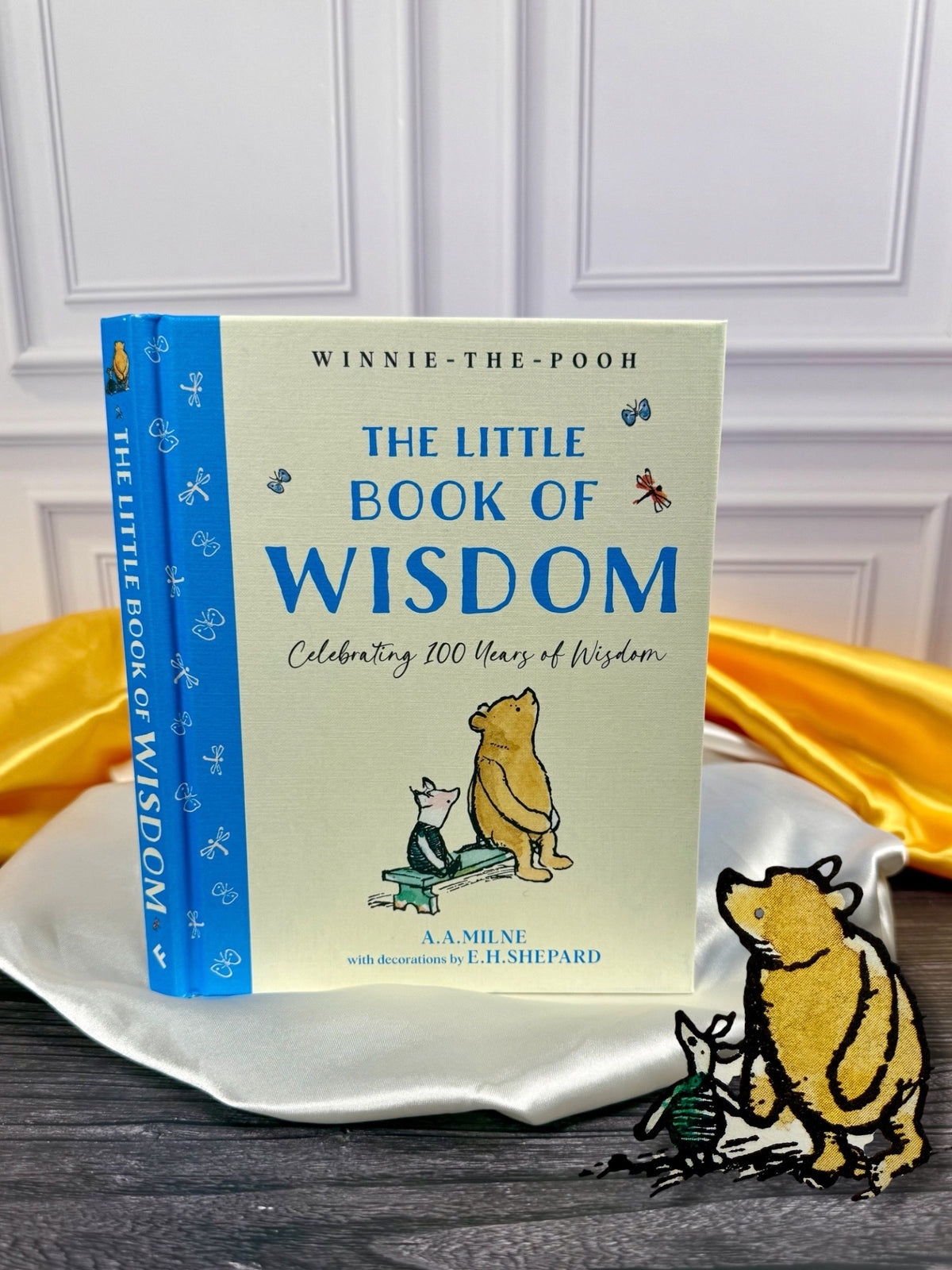 Winnie-the-Pooh: The Little Book of Wisdom by A. A. Milne, illustrated hardcover gift book with pale yellow cover, blue spine, and classic E. H. Shepard Pooh artwork, photographed at StoryGiftStudio™.