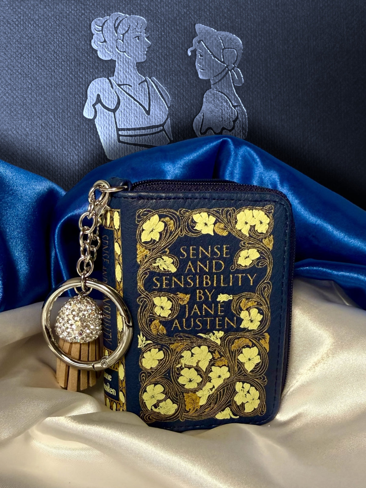 Close-up of Jane Austen Sense and Sensibility book bag charm showing gold floral cover design, zipper, silver keyring, and decorative tassel.