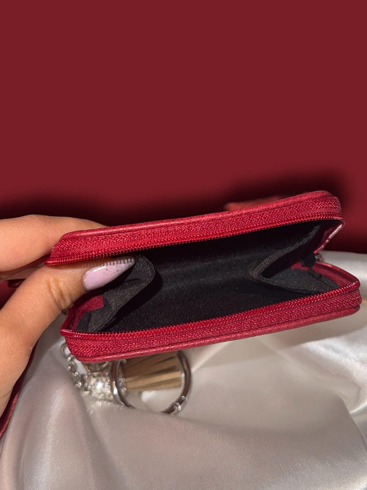 Little Women miniature book coin purse opened to reveal its black interior compartment and red zippered closure, photographed against ivory satin.