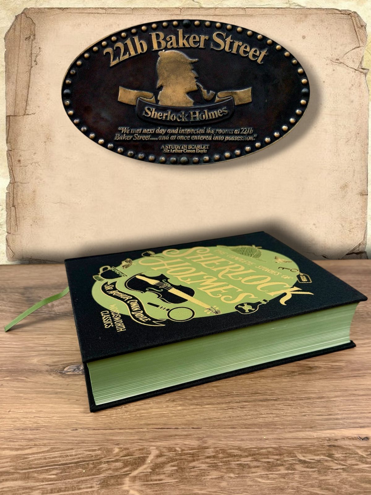 Side view of The Complete Stories of Sherlock Holmes Wordsworth clothbound hardcover resting on a wooden surface, showing green page edges, black fabric binding and green ribbon bookmark.