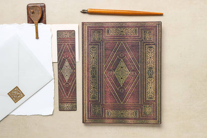Decorative book with ornate cover on a beige surface, accompanied by a pen and envelope.