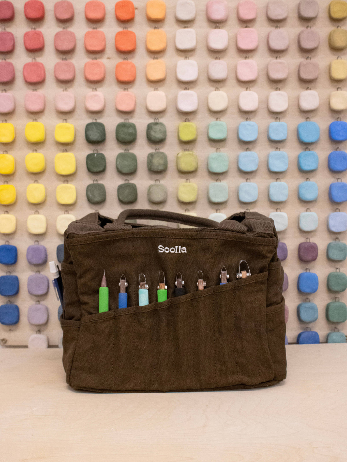 Soolla Studio Bag in Coffee Bean with colorful items against a multicolored square patterned wall