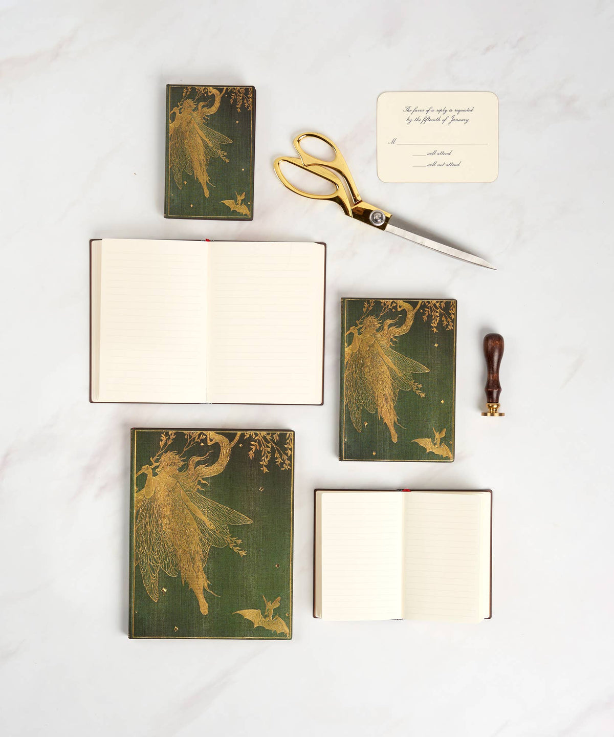 Set of green notebooks with fairy designs, gold scissors, and a sealing wax stamp on a white background