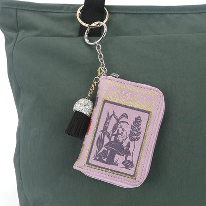 Pink book-shaped keychain with tassel on a green bag