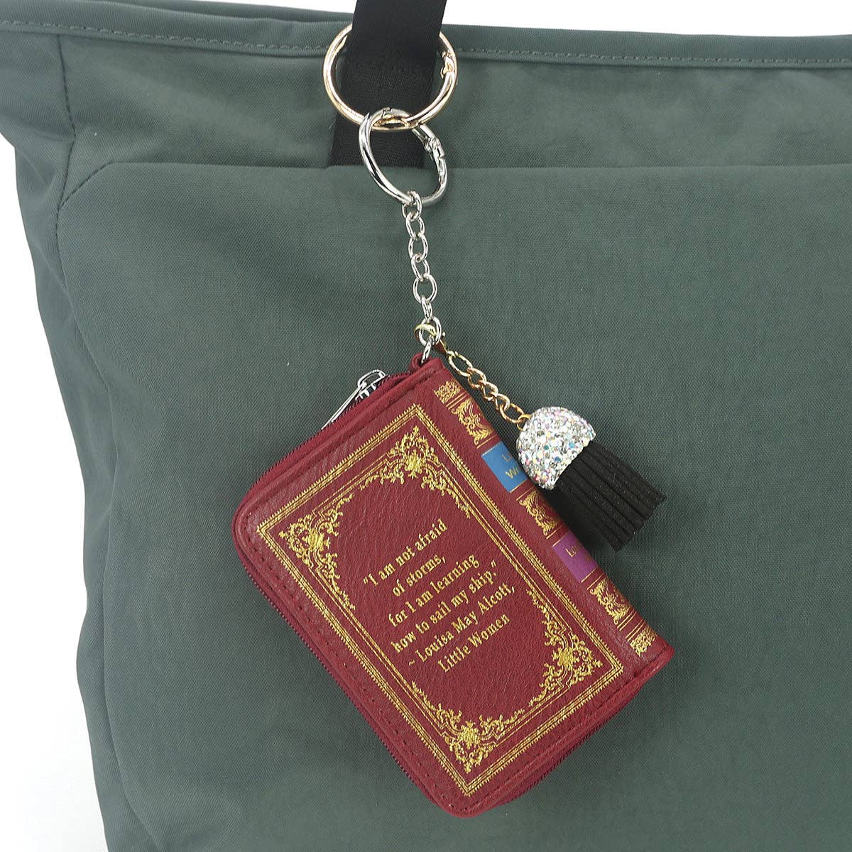 Red book-shaped keychain with gold detailing on a green bag