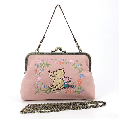Pink Winnie-the-Pooh and Piglet embroidered kisslock handbag with floral design, antique-style metal clasp, wrist strap, and chain shoulder strap.